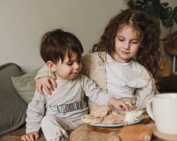 Two young siblings enjoying snacks together on a cozy living room couch, showcasing warmth and togetherness.